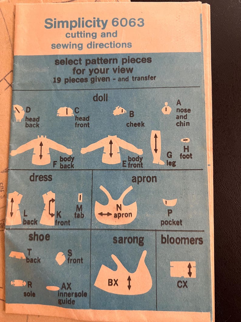 May include: A blue and white sewing pattern guide for Simplicity pattern number 6063. The pattern includes instructions for making a doll, dress, apron, shoe, sarong, and bloomers. The pattern pieces are labeled with letters and names.