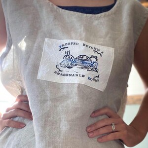 May include: A white linen sleeveless top with a blue and white patch that says "Proofed Beyond a Reasonable Doubt".