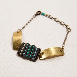 May include: A gold chain bracelet with two hammered metal plates and a woven section of blue, white, and gray beads.