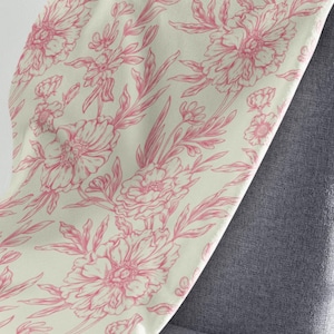 May include: A cream-colored throw blanket with a pink floral pattern. The blanket is made of a soft, plush fabric and features a delicate floral design.