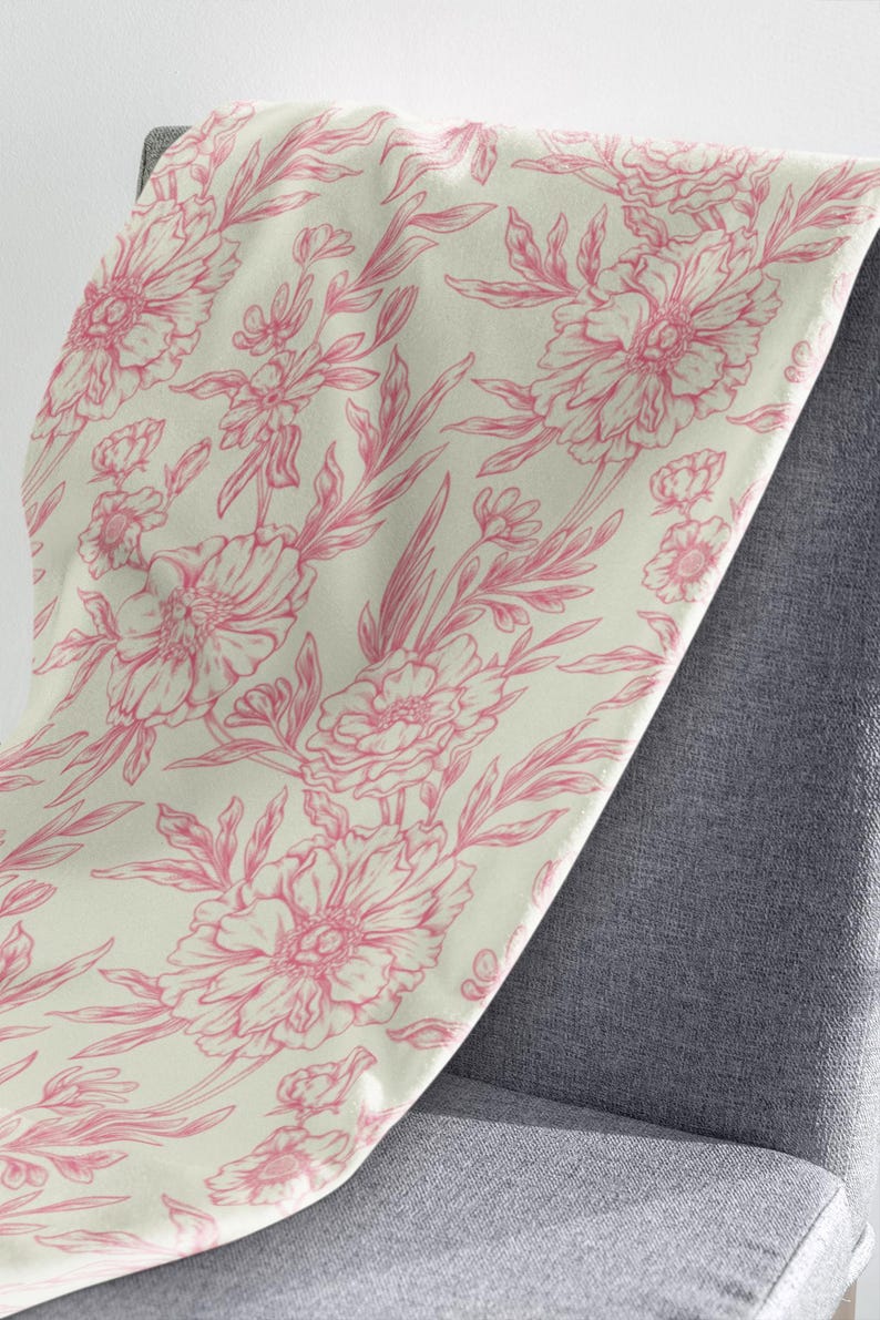 May include: A cream-colored throw blanket with a pink floral pattern. The blanket is made of a soft, plush fabric and features a delicate floral design.