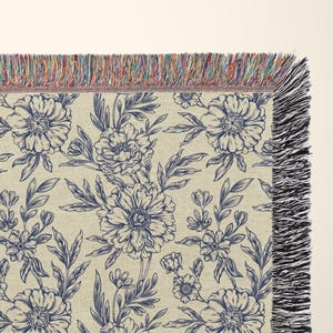 May include: A woven throw blanket with a navy blue floral pattern on a cream background. The blanket has a fringe border.