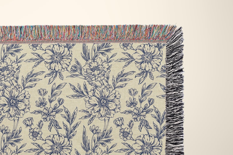 May include: A woven throw blanket with a navy blue floral pattern on a cream background. The blanket has a fringe border.