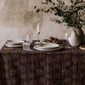 May include: A dining table set for a meal, featuring a dark brown tablecloth with a floral pattern. The table is set with white plates, glasses, and a vase of flowers. A lit candle adds ambiance to the scene.