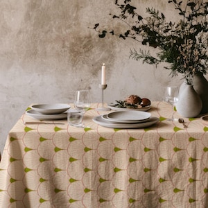 Può includere: Un tavolo da pranzo apparecchiato per un pasto, con una tovaglia fantasia con disegni a ventaglio verdi e rosa. Il tavolo è apparecchiato con piatti grigi, bicchieri e una candela. Una sedia di legno è visibile a sinistra.