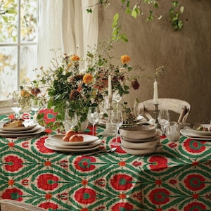 Könnte beinhalten: Ein Esstisch mit einer grün-roten Tischdecke, Tellern, Gläsern und einem Blumengesteck. Der Raum hat eine rustikale Ästhetik mit einem Fenster und einer neutral getönten Wand. Die Tischdekoration deutet auf eine Mahlzeit hin.