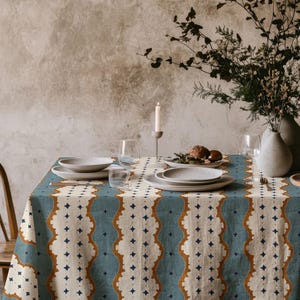 Può includere: Un tavolo da pranzo apparecchiato per un pasto, con una tovaglia a fantasia blu e crema. Il tavolo è apparecchiato con piatti bianchi, bicchieri e un vaso di fiori. Una candela accesa contribuisce all'atmosfera.