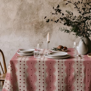 以下が含まれることがあります： 赤とベージュの模様のテーブルクロスが敷かれたダイニングテーブル。白いお皿、グラス、花瓶、ろうそくが置かれ、食事の準備が整っています。