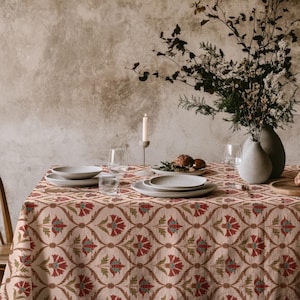 Könnte beinhalten: Ein Esstisch für eine Mahlzeit, mit einer gemusterten Tischdecke in Rot, Grün und Beige. Der Tisch ist mit Tellern, Gläsern und einer Vase mit Blumen gedeckt. Eine brennende Kerze trägt zum Ambiente bei.