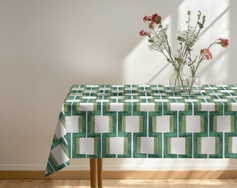 Könnte beinhalten: Eine rechteckige Tischdecke mit einem sich wiederholenden geometrischen Muster aus ineinandergreifenden dunkelgrünen und hellgrünen Linien auf weißem Grund. Zwei klare Glasvasen mit rosa Blumen und weißem Schleierkraut stehen auf dem Tisch.