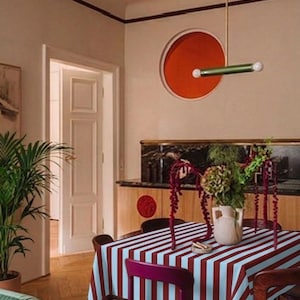 Peut inclure: Intérieur de salle à manger avec une table recouverte d'une nappe à rayures rouges et blanches. Un vase de fleurs est posé sur la table, entouré de chaises. Un luminaire moderne est suspendu au-dessus de la table.