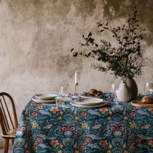 May include: A blue and white tablecloth with a floral and sea creature pattern. The tablecloth is set with plates, glasses, and a candle. The tablecloth is on a table in front of a textured wall.