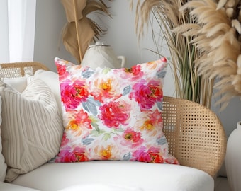 May include: A square throw pillow featuring a watercolor floral pattern with vibrant pink, coral, and orange blossoms set against a white background, accented by soft gray-green leaves and stems throughout the design on the fabric surface.