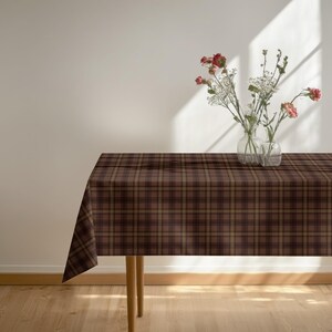 May include: A rectangular table covered with a dark brown and tan plaid tablecloth. Two clear glass vases sit on the surface, each containing a small arrangement of delicate pink flowers and white baby's breath stems.