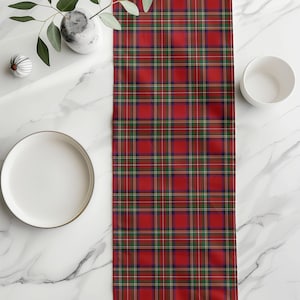 Pode incluir: Um caminho de mesa xadrez vermelho, verde e azul. O caminho de mesa é retangular e apresenta um padrão de tartan clássico. O caminho de mesa é exibido em uma superfície de mármore branco, com um prato e uma tigela brancos visíveis.