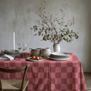 Könnte beinhalten: Ein Esstisch, gedeckt mit einer rot karierten Tischdecke. Der Tisch ist mit Tellern, Schalen, Gläsern und einer Vase mit Blumen gedeckt. Eine brennende Kerze und ein Holzstuhl sind ebenfalls zu sehen.
