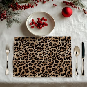 May include: A rectangular placemat featuring a brown, tan, and black leopard print pattern. The placemat is positioned on a white tablecloth, accompanied by a silver fork on the left and a silver spoon and knife on the right side.