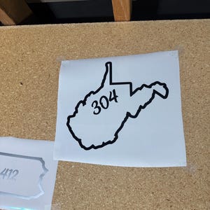May include: A white sticker with a black outline of the state of West Virginia and the number 304 printed inside.
