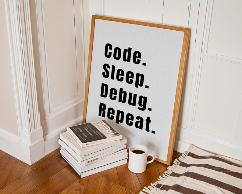 Peut inclure: Une impression encadr&eacute;e avec le texte "Code. Sleep. Debug. Repeat." sur un fond blanc. Le cadre est en bois et a une finition naturelle. L'impression est appuy&eacute;e contre un mur blanc, et il y a quelques livres empil&eacute;s sur un sol en bois devant elle.