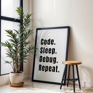 Peut inclure: Affiche encadr&eacute;e noire avec le texte "code. sleep. debug. repeat." accroch&eacute;e &agrave; un mur blanc &agrave; c&ocirc;t&eacute; d'une plante en pot et d'un tabouret en bois avec des pieds noirs.