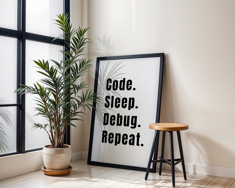 Peut inclure: Affiche encadr&eacute;e noire avec le texte "code. sleep. debug. repeat." accroch&eacute;e &agrave; un mur blanc &agrave; c&ocirc;t&eacute; d'une plante en pot et d'un tabouret en bois avec des pieds noirs.