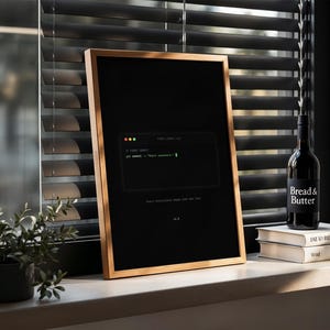 Puede incluir: Un p&oacute;ster vertical enmarcado con fondo negro que presenta un gr&aacute;fico de ventana de terminal con el texto git commit -m "Start somewhere." y la frase Every masterpiece begins with one line. El marco es de madera clara fina.