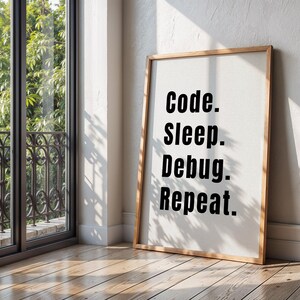 Peut inclure: Une impression encadr&eacute;e avec le texte "Code. Sleep. Debug. Repeat." en lettres noires sur fond blanc. Le cadre est en bois et a une finition brun clair.