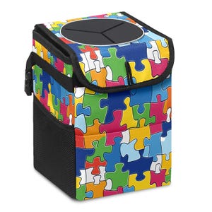 May include: A colorful car trash can featuring a jigsaw puzzle pattern in shades of blue, green, yellow, orange, and pink. The trash can has a black lid with a circular opening and a black mesh side pocket. A black handle and buckle are visible.