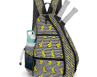 May include: A black and white striped backpack with a yellow banana pattern. The backpack has a side pocket with a water bottle and two tennis rackets. The backpack is designed for sports and outdoor activities.
