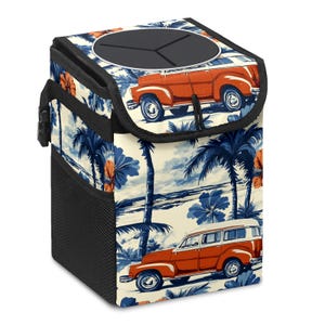May include: A car waste bin with a tropical design. The bin has a cream background with blue palm trees, orange hibiscus flowers, and orange vintage cars. The top has a black lid with three openings and a black handle.