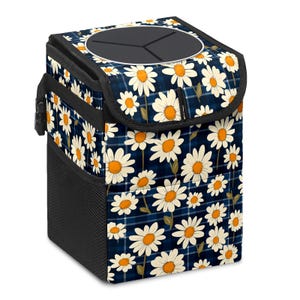 May include: A square car trash can with a daisy floral pattern on a navy blue plaid background. The trash can has a black mesh side pocket and a black lid with a circular opening.