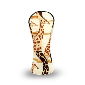 May include: A golf club head cover featuring a giraffe design. The cover is primarily cream-colored with a repeating pattern of giraffes in shades of brown. The top edge is trimmed with black.