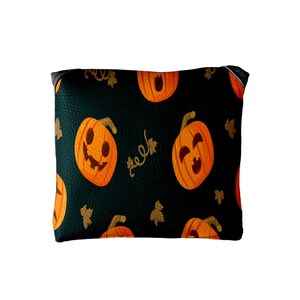 May include: A black Halloween-themed pouch with a repeating pattern of orange jack-o'-lanterns, gold leaves, and vines. The pouch has a black zipper and is made of a textured material.
