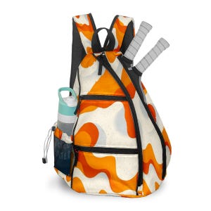 Peut inclure: Sac à dos de tennis avec un motif abstrait blanc, orange et noir. Le sac à dos a une bouteille d'eau dans la poche latérale et deux raquettes de tennis. La bouteille d'eau est bleu clair et grise. Le sac à dos a une fermeture éclair et des bretelles noires.