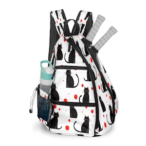 Puede incluir: Una mochila blanca con un estampado de gato negro y lunares rojos. La mochila tiene un bolsillo para botella de agua y lleva dos raquetas de tenis. El texto en el bolsillo de la botella de agua dice "FILTERED WATER".
