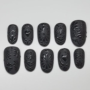 May include: Ten black oval-shaped false nails with intricate floral and heart designs.