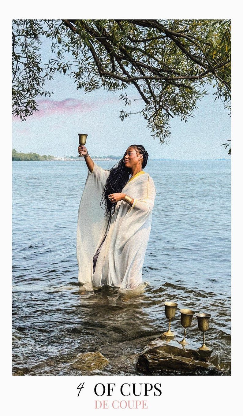 May include: A person wearing a white, flowing, sheer robe with gold trim, standing in water while holding a gold chalice aloft. Three additional gold chalices are positioned on a rock in the foreground. The text 4 OF CUPS DE COUPE is at the bottom.
