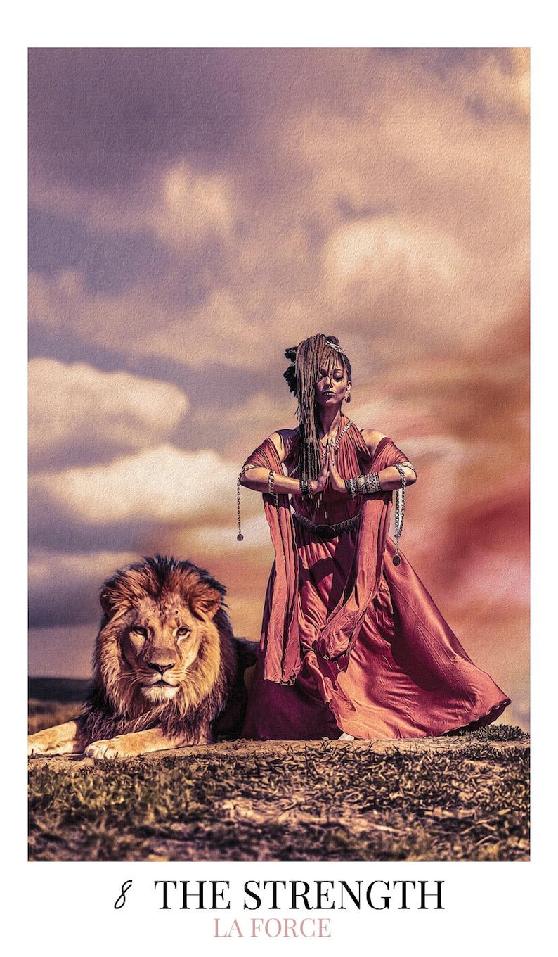May include: A tarot card featuring a person with dreadlocks wearing a flowing rust-colored dress with arms in a prayer position, standing beside a large male lion. The text 8 THE STRENGTH LA FORCE is printed at the bottom of the card.