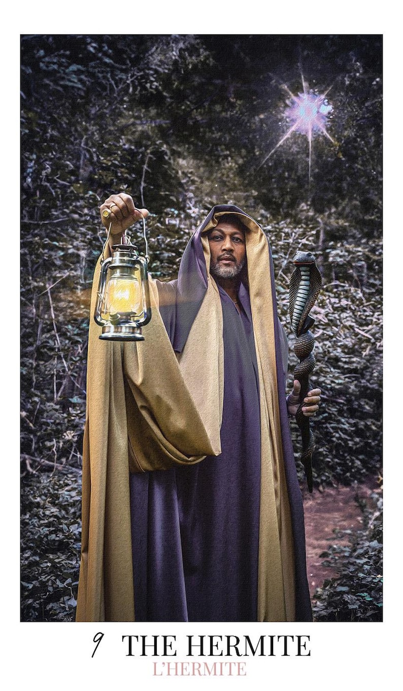 May include: A person wearing a purple and gold hooded robe, holding a lit metal lantern in one hand and a dark staff topped with a cobra figure in the other. The text "9 THE HERMITE L'HERMITE" is printed at the bottom of this tarot card image.