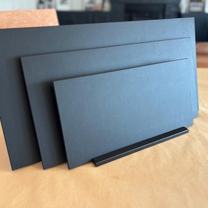 May include: Three black rectangular signs with a black stand. The signs are stacked on top of each other, with the largest sign at the bottom and the smallest sign at the top.