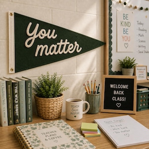 Könnte beinhalten: Ein dunkelgrüner Filzwimpel mit dem weißen Text You matter, ein geflochtener Korb mit einer grünen Pflanze, eine weiße Tasse mit dem Text Teach love inspire, ein schwarzes Buchstabenbrett mit dem Text Welcome back class und ein Notizbuch.