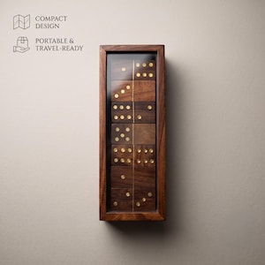 May include: A rectangular wooden box with a clear lid containing a set of dark brown wooden dominoes with gold-colored pips. The text COMPACT DESIGN and PORTABLE & TRAVEL-READY is visible on the left side of the image.