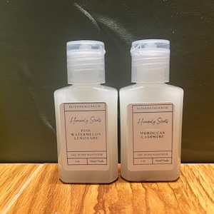 Puede incluir: Dos botellas de plástico transparente de desinfectante de manos con etiquetas blancas. Las etiquetas tienen el texto "ALISEDESIGNSCO Heavenly Scents" y las fragancias son "Pink Watermelon Lemonade" y "Moroccan Cashmere".