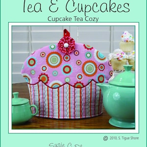Peut inclure: Un chauffe-thé en forme de cupcake rose avec un motif floral et une fleur rouge sur le dessus. Un service à thé vert est à côté. Le texte "Tea & Cupcakes" et "Cupcake Tea Cozy" sont visibles.