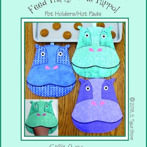 May include: Four quilted pot holders shaped like hippos in blue, green, purple and turquoise. The pot holders have a checkered pattern and embroidered eyes and noses. The text "Feed Happy The Hippo!" and "Pot Holders/Hot Pads" is at the top of the image. The text "ST-1812" is in the top right corner. The text "Susie C Shore Designs" is at the bottom of the image.