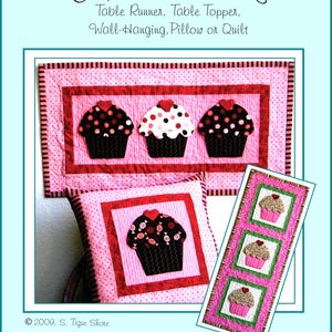 Può includere: Un modello di trapunta per un runner da tavolo, un topper da tavolo, un'appendice da parete, un cuscino o una trapunta a tema cupcake. Il modello presenta uno sfondo rosa con accenti rossi e bianchi e tre cupcake con diversi design.