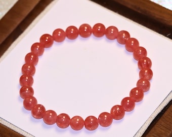 May include: A circular stretch bracelet composed of polished, translucent red gemstone beads. The beads are uniform in size and shape, creating a continuous loop. The text "Charming Cosmic Crafts" is printed in small black letters at the bottom.