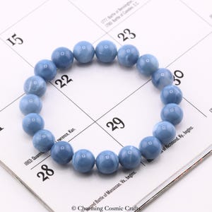 May include: A bracelet made of round, light blue beads. The beads have a marbled appearance and are strung together to form a circular shape. The bracelet is resting on a calendar page with numbers and text.