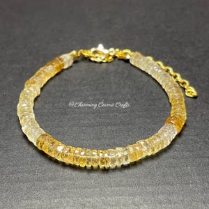 Puede incluir: Un brazalete dorado con cierre de cadena, hecho con pequeñas cuentas de citrino facetadas, de color amarillo claro y transparentes.