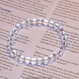 May include: A clear quartz crystal bracelet with faceted beads. The bracelet is lying on a page of text that includes the words "Consider" and "An Example".